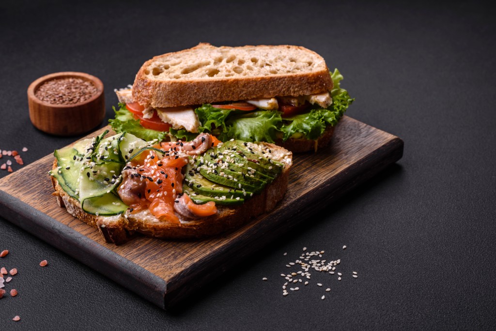 Fresh tasty sandwich with salmon, avocado and sesame and flax seeds on a dark concrete background