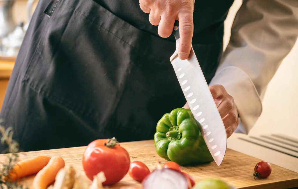Chef with black apron cutting green pepper on a chopping board